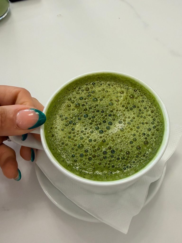 Hand holding a matcha latte in a white cup on a marble surface, morning wellness ritual for women over 40