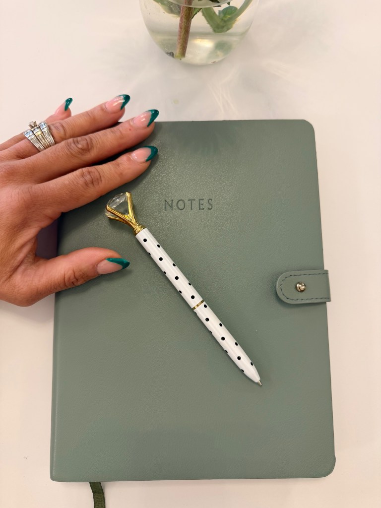 Hand resting on a sage green journal with a diamond pen, intentional living and personal growth for women over 40